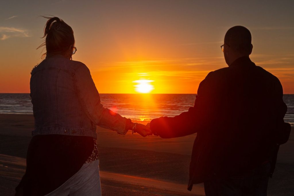 Photo d'un couple en bord de mer, face au coucher de soleil.