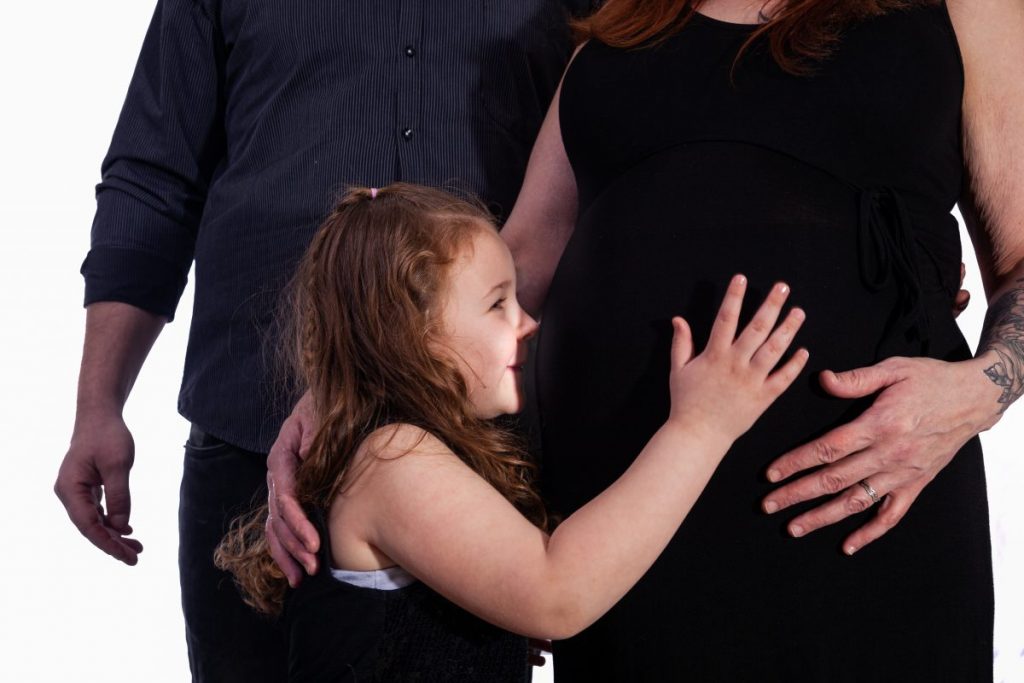 les parent et la soeur touchant le ventre rond de la maman