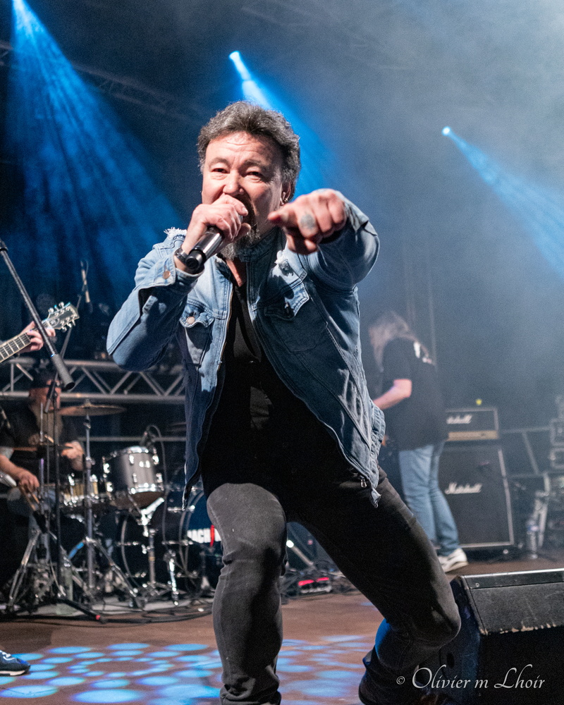 chanteur de hardrock pointant du doigt l'objectif sur scène