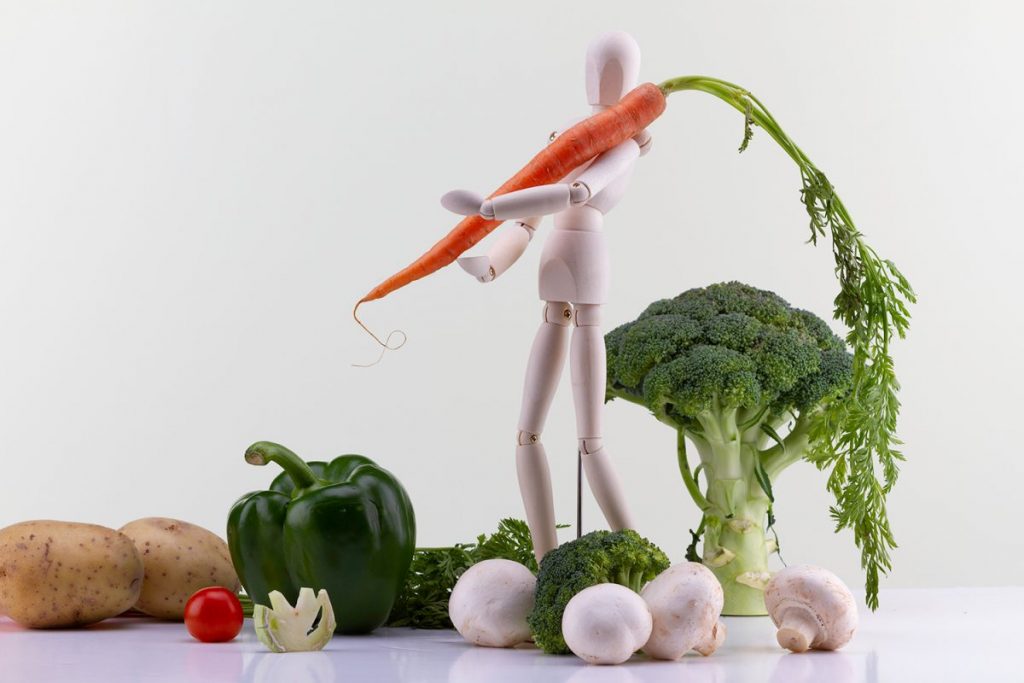 pantin en studio, portant des fruit et legume, le décors est une nature morte composée de legumes donnant un effet de paysage autour