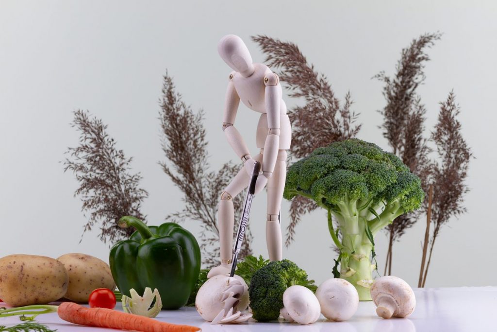 pantin en studio, portant des fruit et legume, le décors est une nature morte composée de legumes donnant un effet de paysage autour