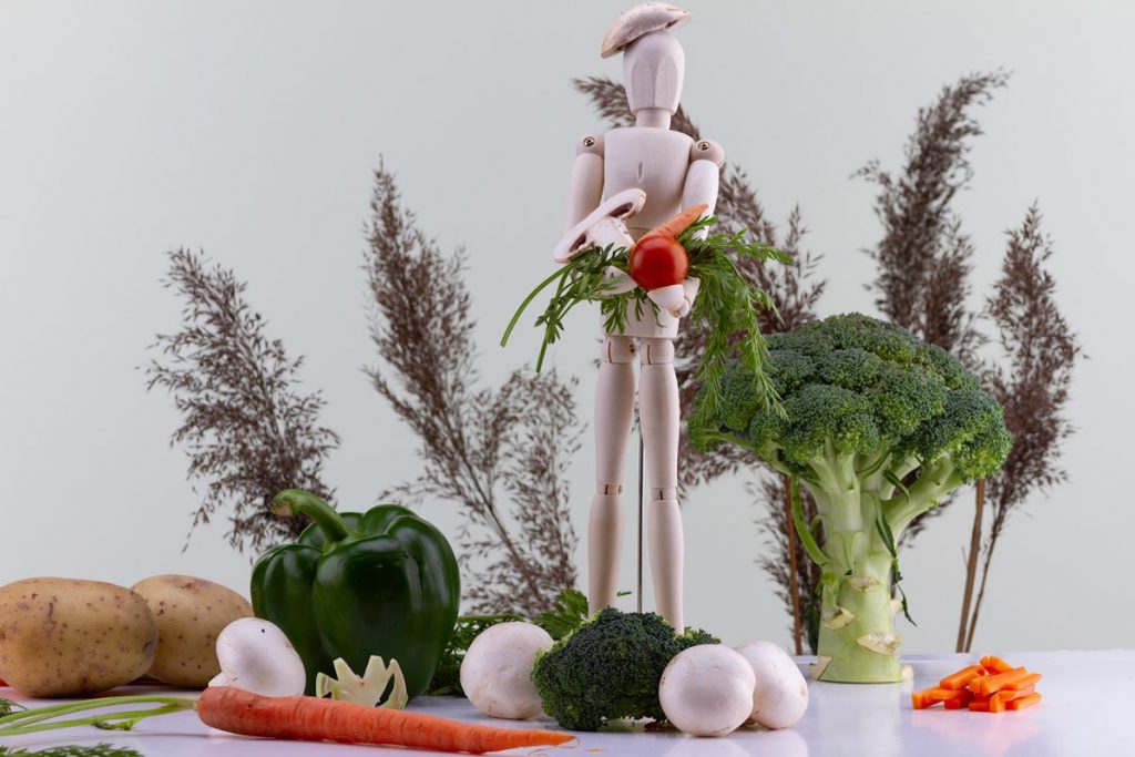 pantin en studio, portant des fruit et legume, le décors est une nature morte composée de legumes donnant un effet de paysage autour
